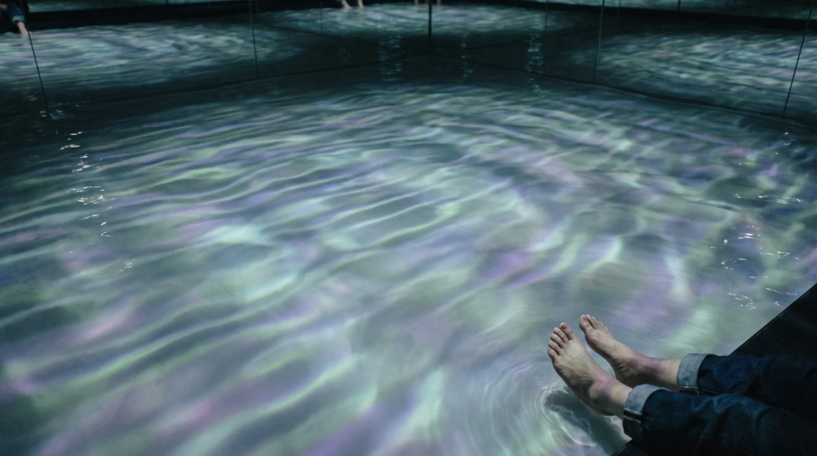 Visitors wading barefoot through a mirrored water room at teamLab Planets in Toyosu, Tokyo, Japan