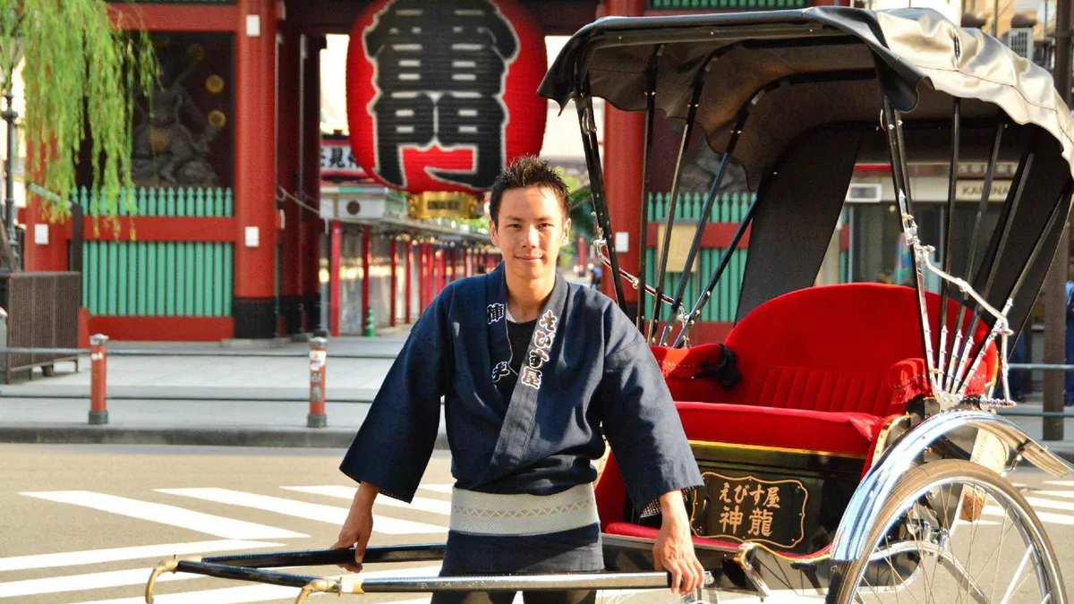 Tourists riding a traditional rickshaw past Asakusa Shrine and cherry trees near Sumida Park, Tokyo Japan