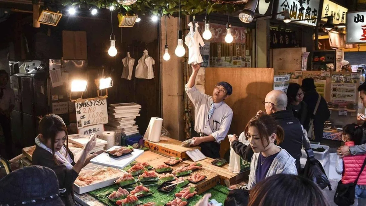 Guide leading visitors past seafood stalls in Tsukiji Outer Market ahead of a teamLab Planets museum visit, Tsukiji and teamLab Planets tour
