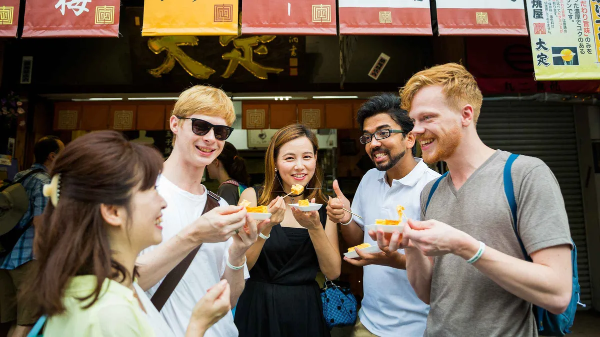 Guide handing a skewer of Wagyu beef to travelers on a Tsukiji Outer Market food tasting tour in Tokyo