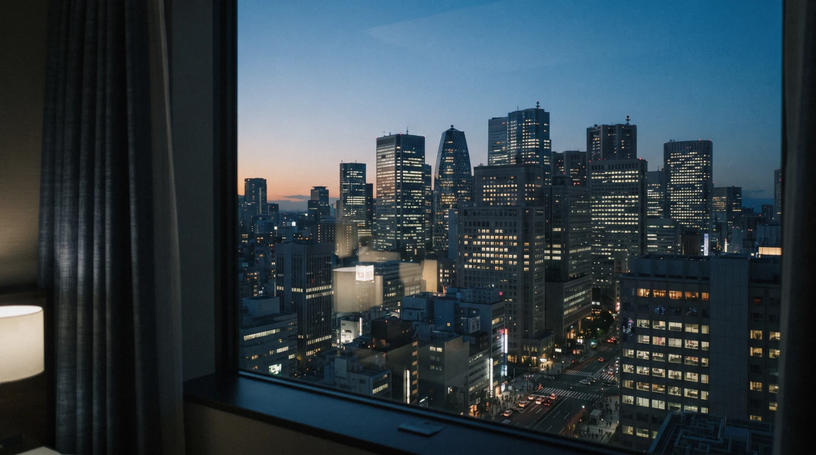Lit hotel windows above a quiet side street of low buildings and vending machines at dusk, choosing where to stay in Tokyo